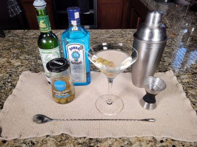 A gin martini in a martini glass surrounded by the items used to make it.