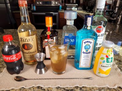 A Long Island iced tea in a tall glass surrounded by the items used to make it.