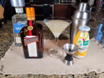 A margarita in a martini glass surrounded by the items used to make it.